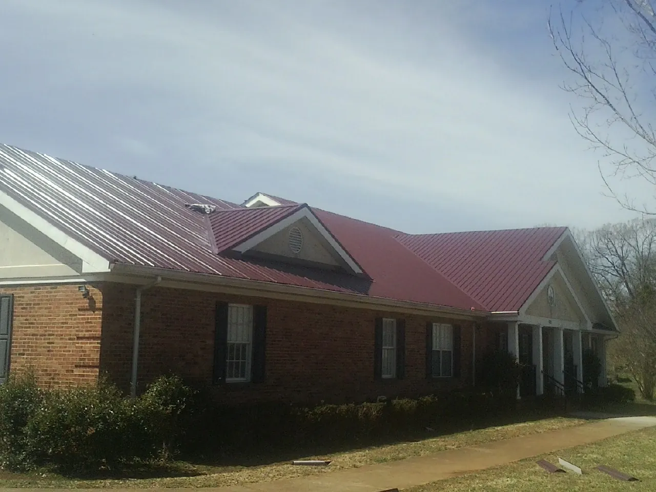 Red metal roof with gabled entries on a long brick building, from a Hail Damage Roof Repair job in Hollandale