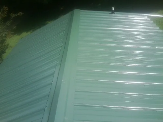 New green metal panels meeting at the ridge of a roof — Flat Roof Repair work by our crew in Hollandale