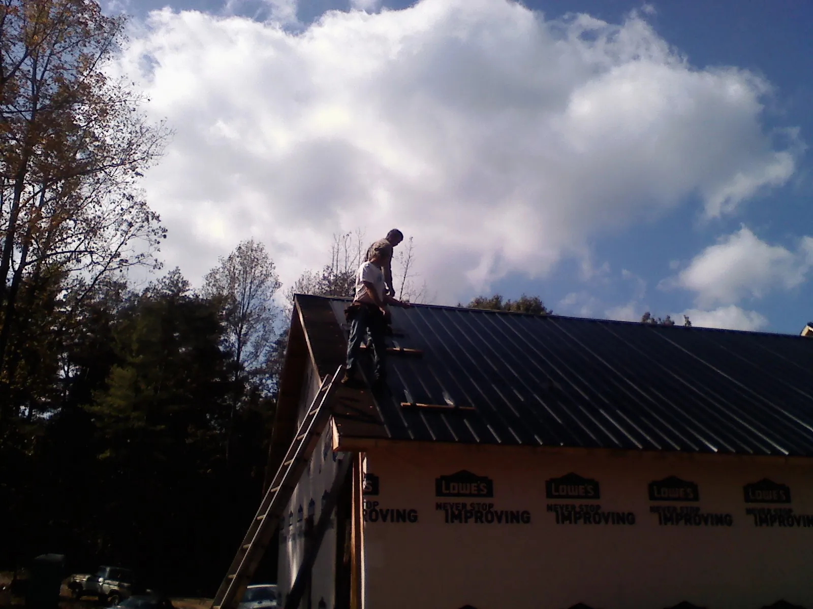 Roofer fastening dark metal panels high against a cloudy sky, from a Roof Inspection job in Hollandale