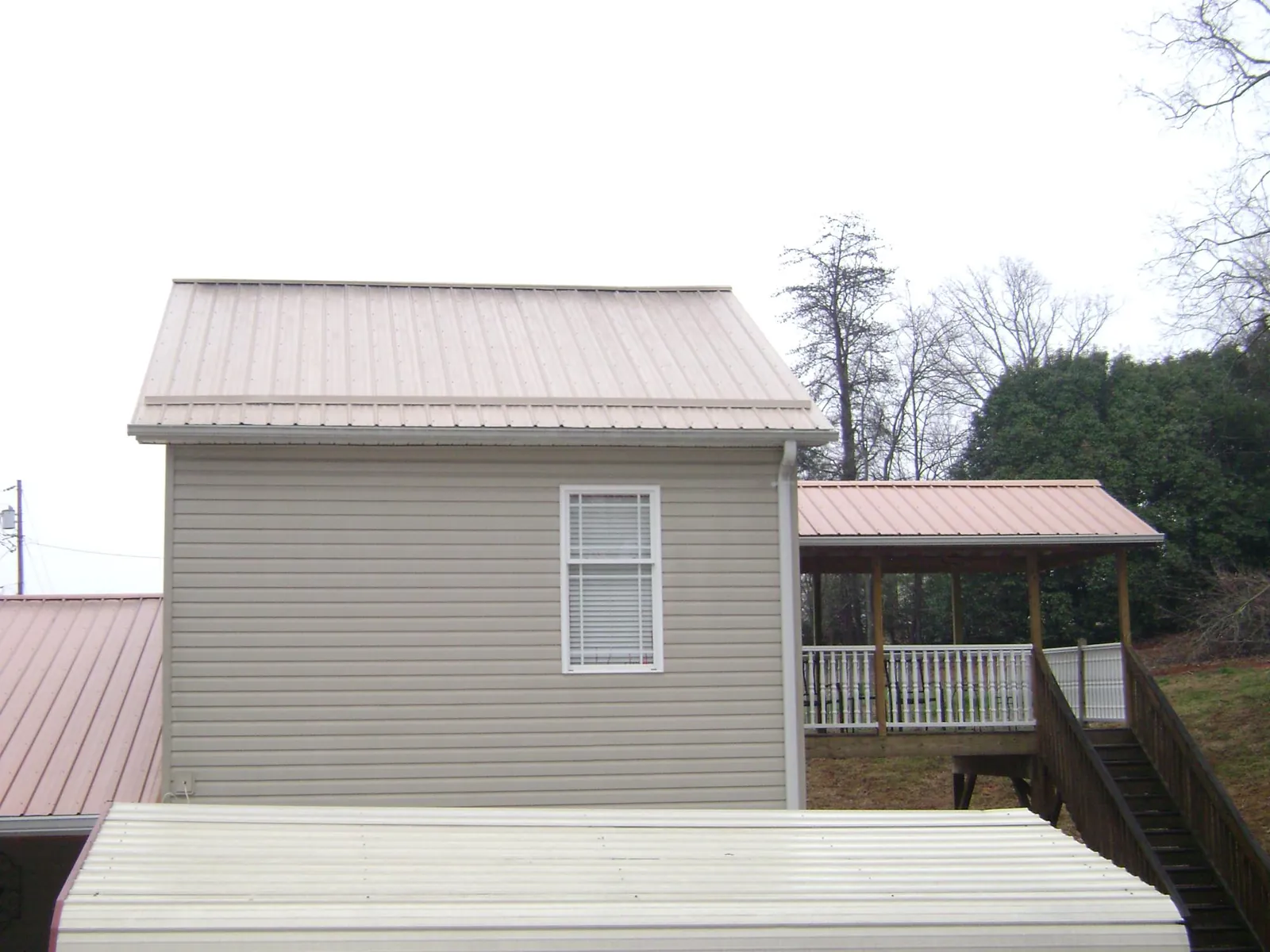 Tan metal roofs on a two story addition and attached porch, from a Roof Replacement job in Hollandale